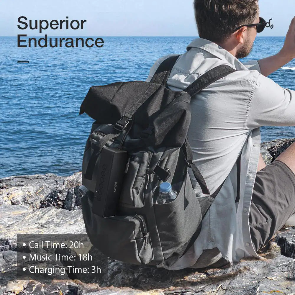 A person wearing a white shirt sits on coastal rocks with a black backpack containing the Xdobo speaker. Text overlay reads 'Superior Endurance' with battery specifications.