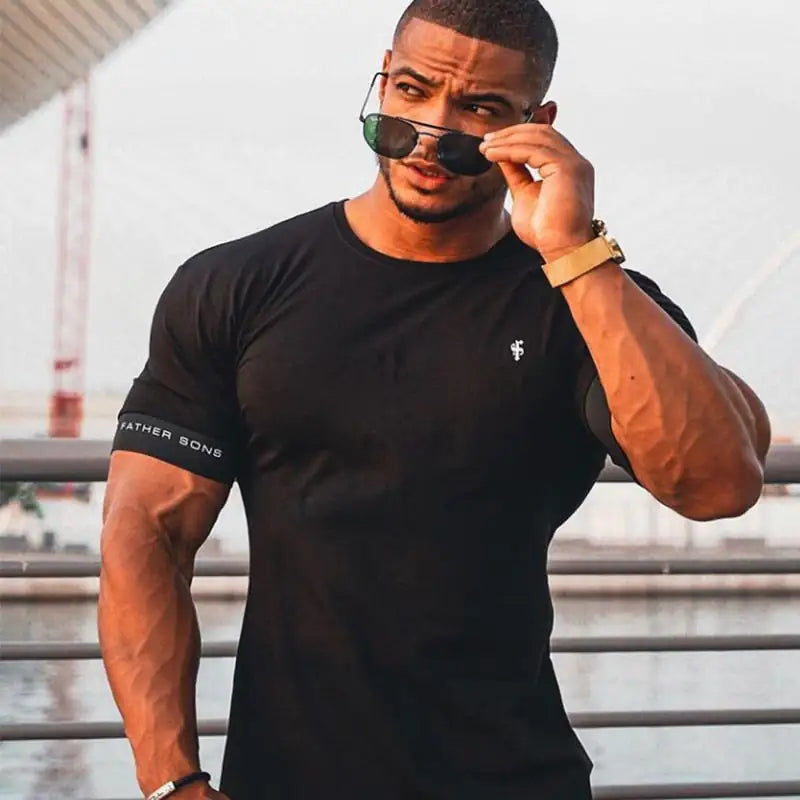 Athletic man in black Father Sons t-shirt adjusting sunglasses, wearing gold watch and ring in urban setting