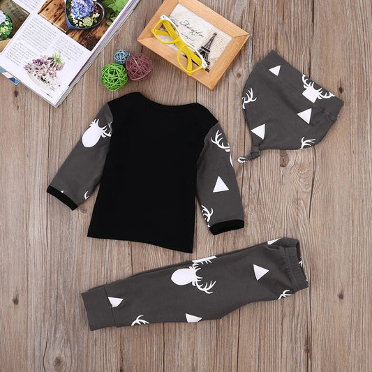 Baby outfit set with deer pattern featuring black/gray top, pants and hat on wooden background