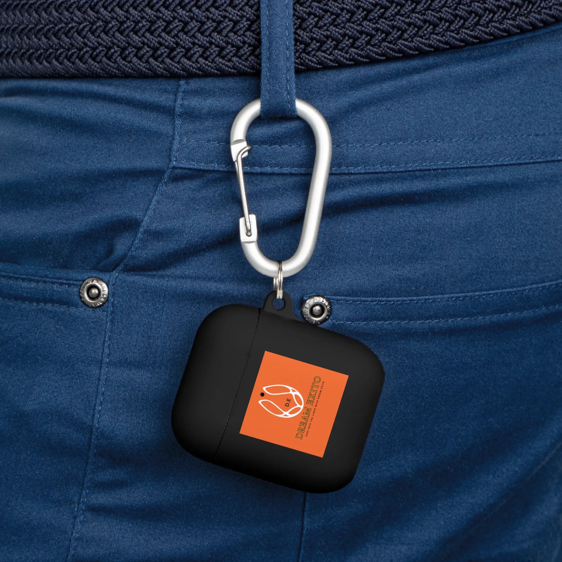 Black AirPods case with an orange logo attached to a blue belt loop using a carabiner.