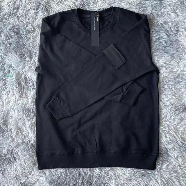 Black cotton sweatshirt with round neckline and black arm patch, displayed on plush gray fur background