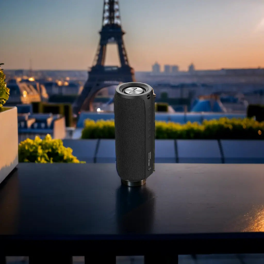 Black portable speaker with the Eiffel Tower in the background during sunset.