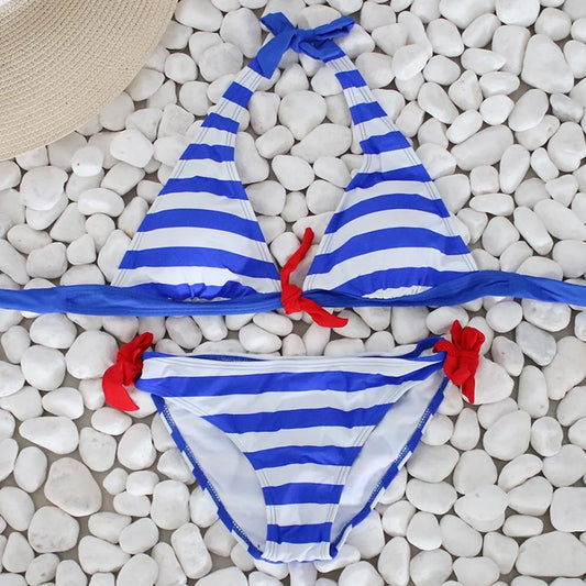 Blue and white striped bikini set with red bow accents displayed on white pebbles, halter top design