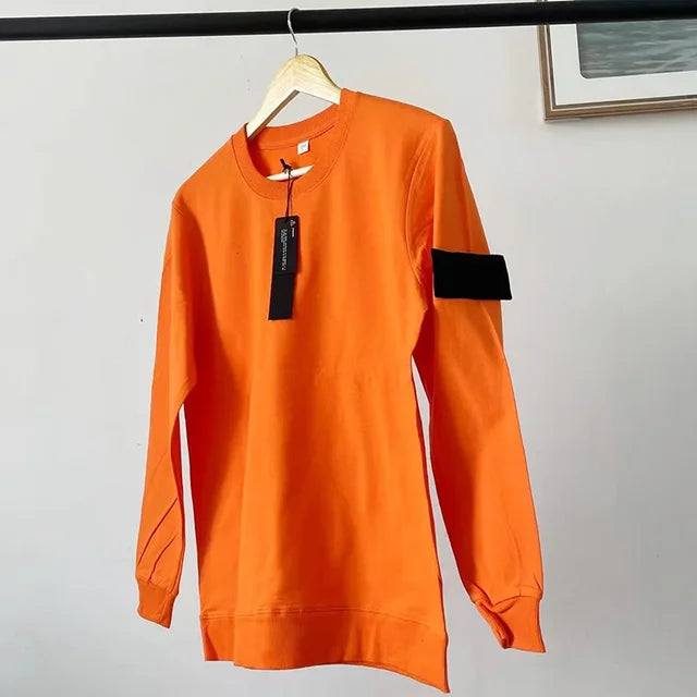 Bright orange crewneck sweatshirt with black rectangular arm patch, hanging on wooden display hanger