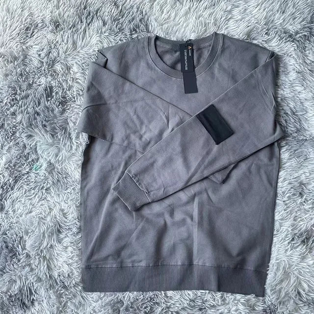 Charcoal gray crewneck sweatshirt with black arm patch, photographed on plush gray fur surface