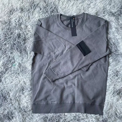 Charcoal gray crewneck sweatshirt with black arm patch, photographed on plush gray fur surface