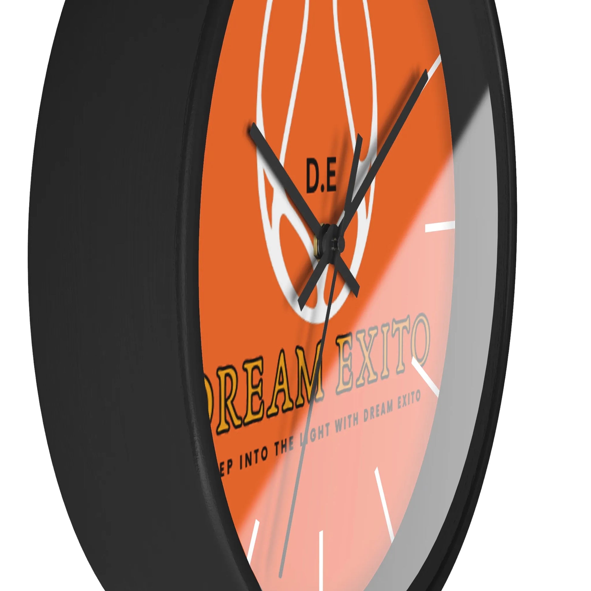 Close-up of a round wall clock with a black frame and orange face displaying "DREAM EXITO.