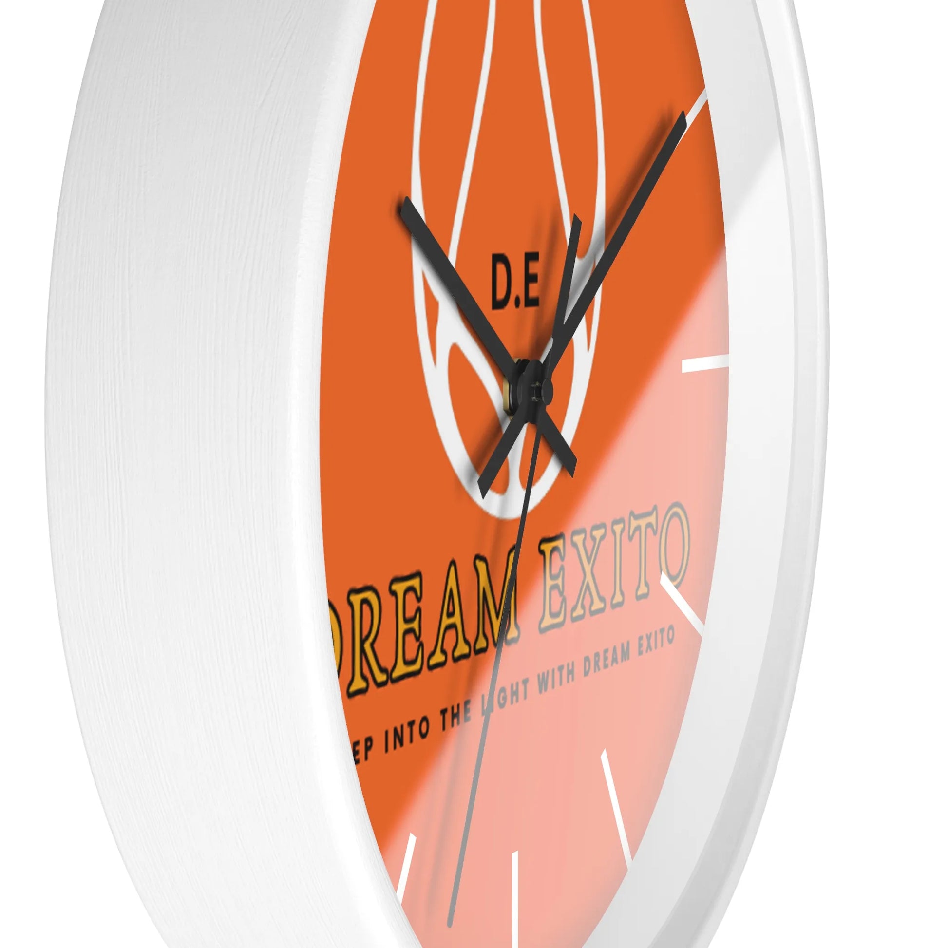 Close-up of a white-framed wall clock with an orange face featuring the text "DREAM EXITO" and a white flame design