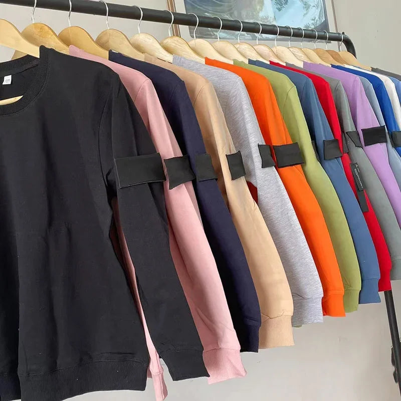 Collection of sweatshirts in various colors hanging on wooden hangers, showing black arm patches