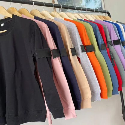 Collection of sweatshirts in various colors hanging on wooden hangers, showing black arm patches