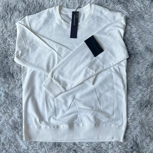 Crisp white crewneck sweatshirt with black arm patch and tag, photographed on plush gray backdrop