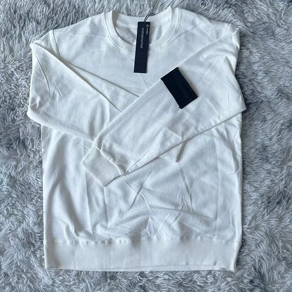 Crisp white crewneck sweatshirt with black arm patch and tag, photographed on plush gray backdrop