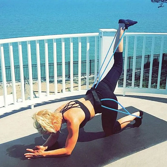 Fitness instructor performs advanced leg and core exercise on oceanfront deck with resistance bands