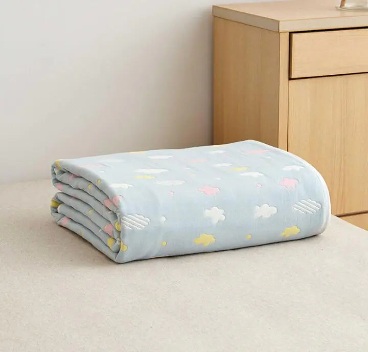 Folded light blue baby blanket with pastel cloud patterns next to wooden dresser.