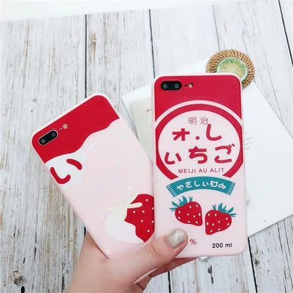 Hand holding two red and pink Japanese-themed phone cases with strawberry designs on wooden surface