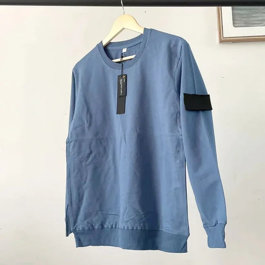 Light blue crewneck sweatshirt with black arm patch, ribbed cuffs and hem, hanging on wooden hanger