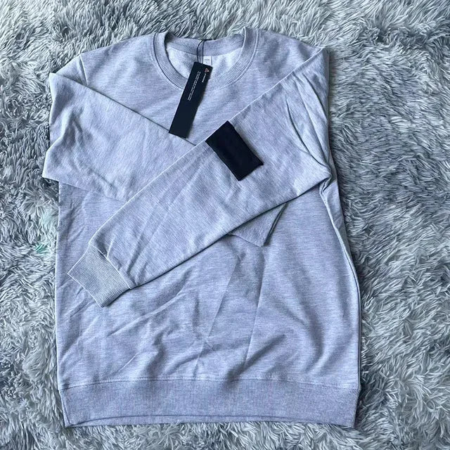 Light gray sweatshirt with black arm patch and price tag, laid flat on plush gray furry background