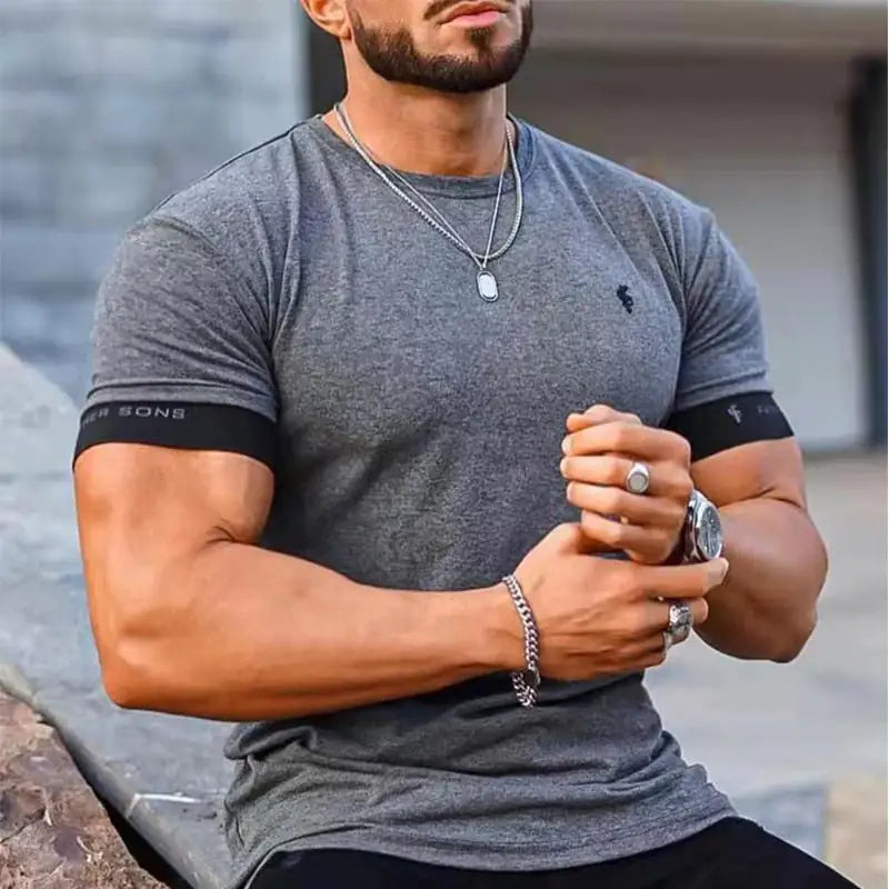 Man in grey fitted t-shirt with Father Sons sleeve detail, wearing jewelry and displaying muscular physique