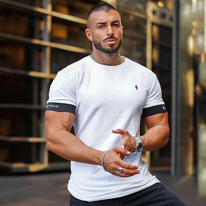 Man in white Father Sons t-shirt with black sleeve bands, wearing chain and watch, modern building backdrop