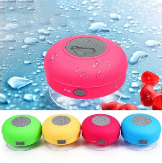 Multicolored waterproof Bluetooth speakers, with the main one in pink on a wet surface.