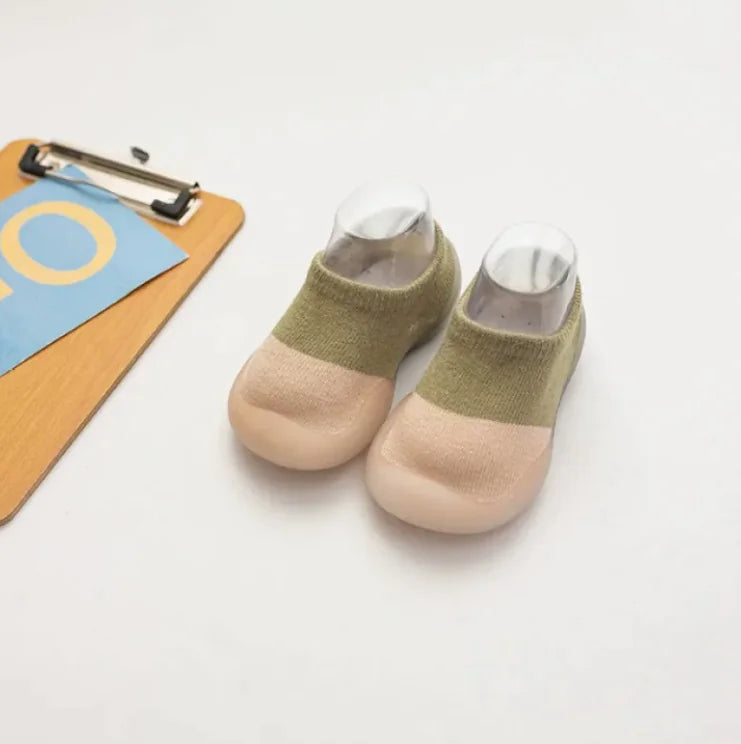 Olive green and beige two-tone baby socks beside wooden clipboard with blue paper on white surface