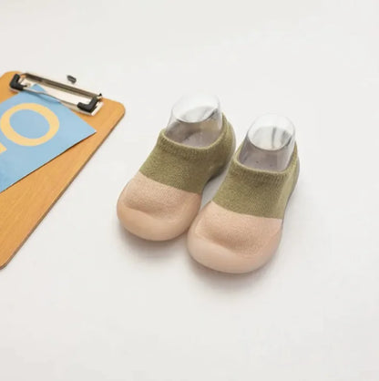 Olive green and beige two-tone baby socks beside wooden clipboard with blue paper on white surface