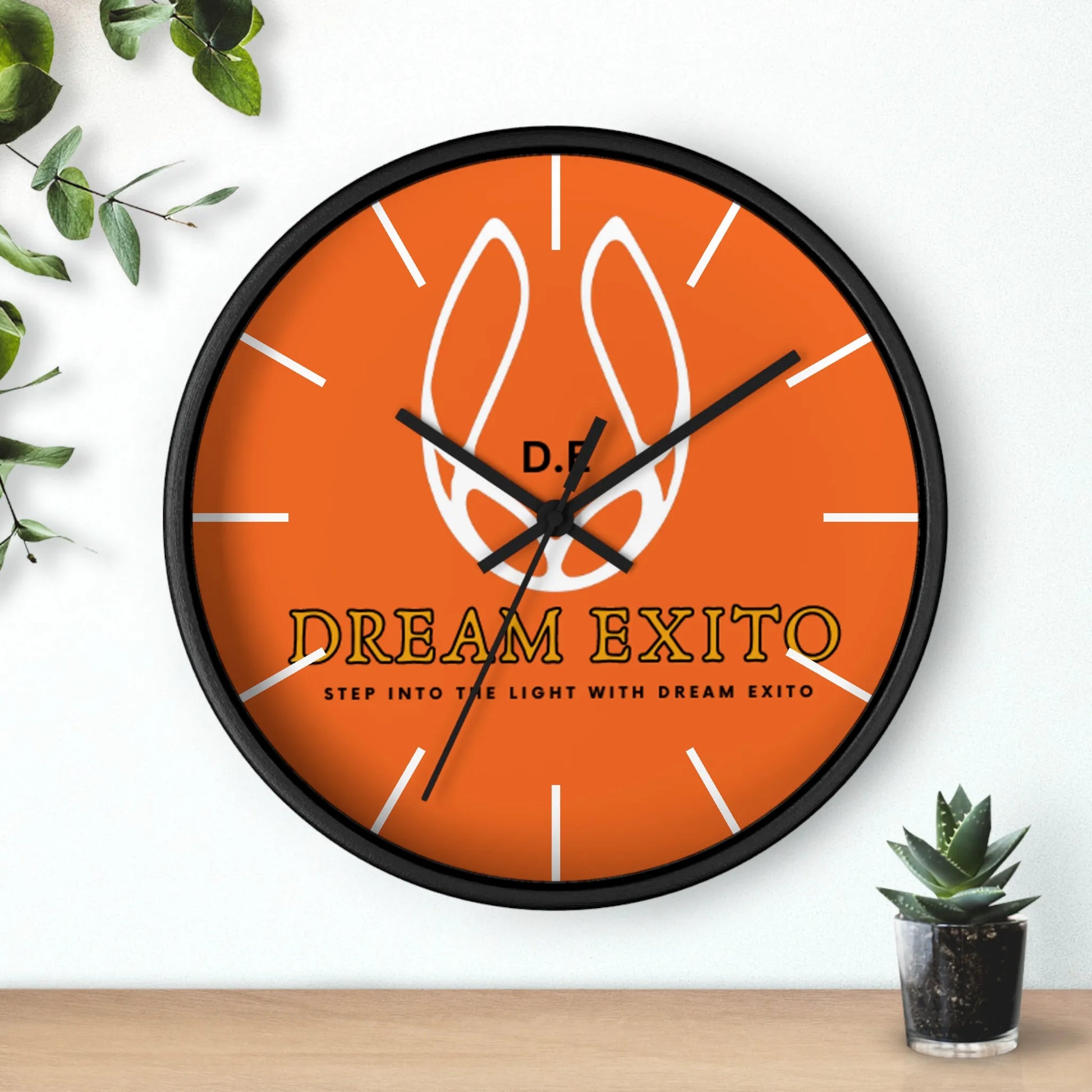 Orange wall clock with black frame, featuring a white flame logo and the words "DREAM EXITO.