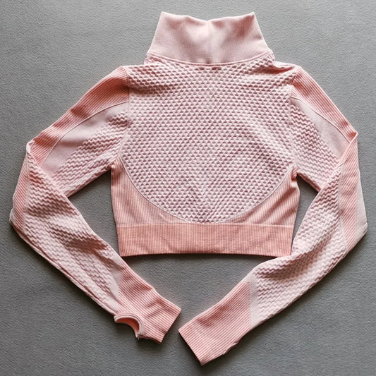 Pale pink cropped athletic jacket with textured honeycomb pattern and ribbed details on a gray background