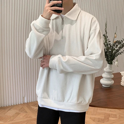 Person in cream ribbed quarter-zip pullover taking mirror selfie, white vase with plants in background