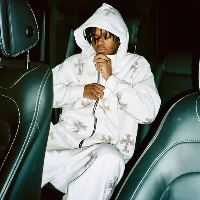 Person in white cross-patterned tracksuit sitting in leather car seat, hand thoughtfully posed near face