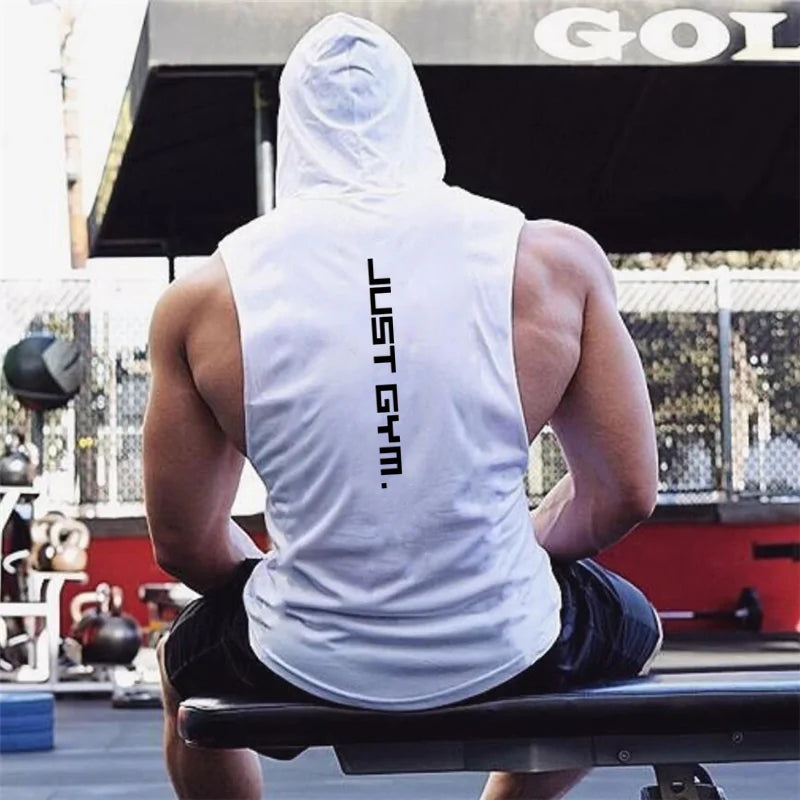 Person wearing white sleeveless hoodie with "JUST GYM" text, sitting at gym bench, equipment visible behind