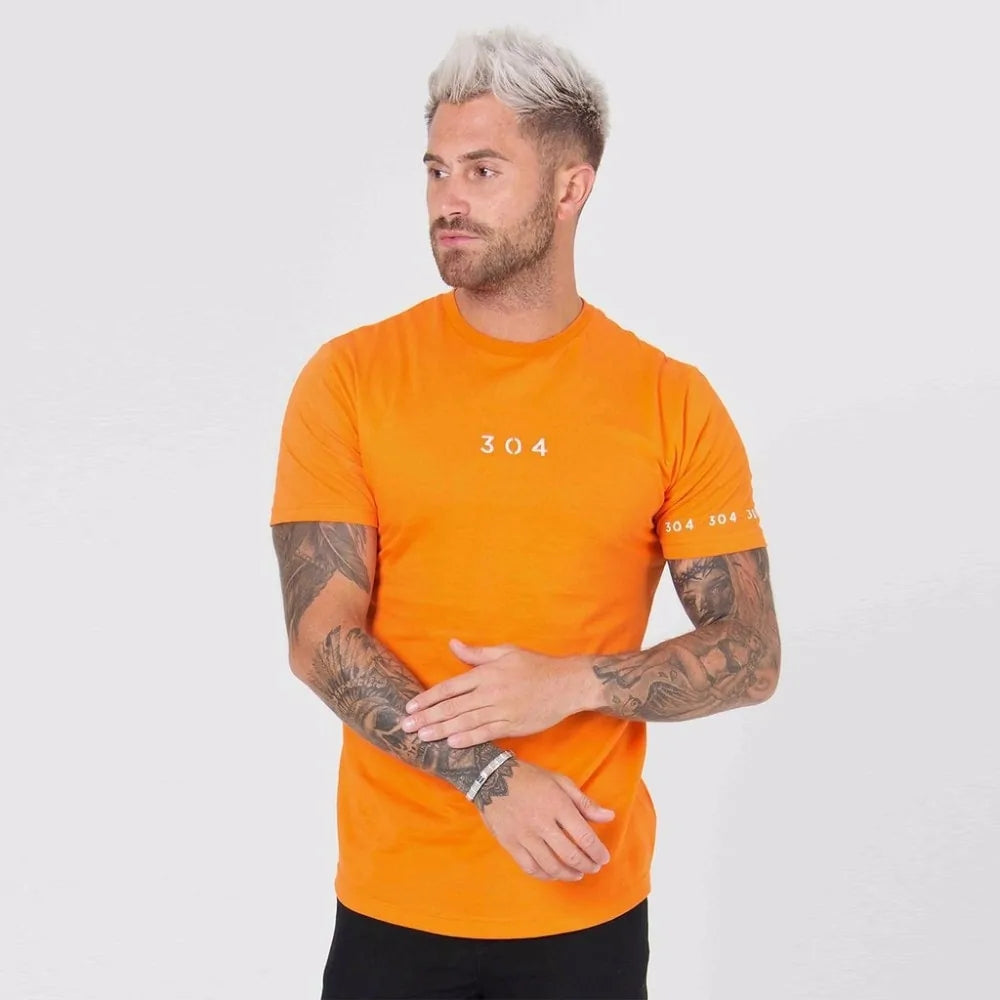 Person with platinum hair and tattoos wearing bright orange t-shirt with "304" logo and slim jeans