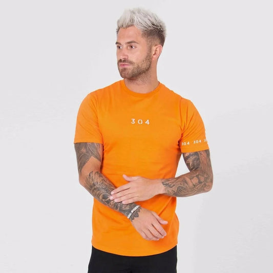 Person with platinum hair and tattoos wearing bright orange t-shirt with "304" logo and slim jeans