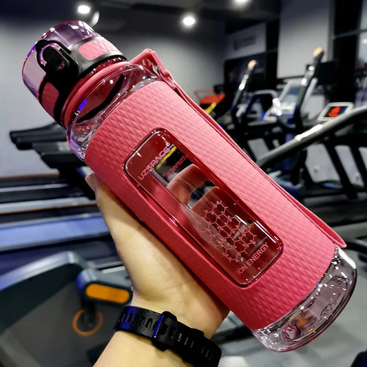 Pink UZSPACE water bottle with textured sleeve and ion energy filter held in gym, treadmills behind.