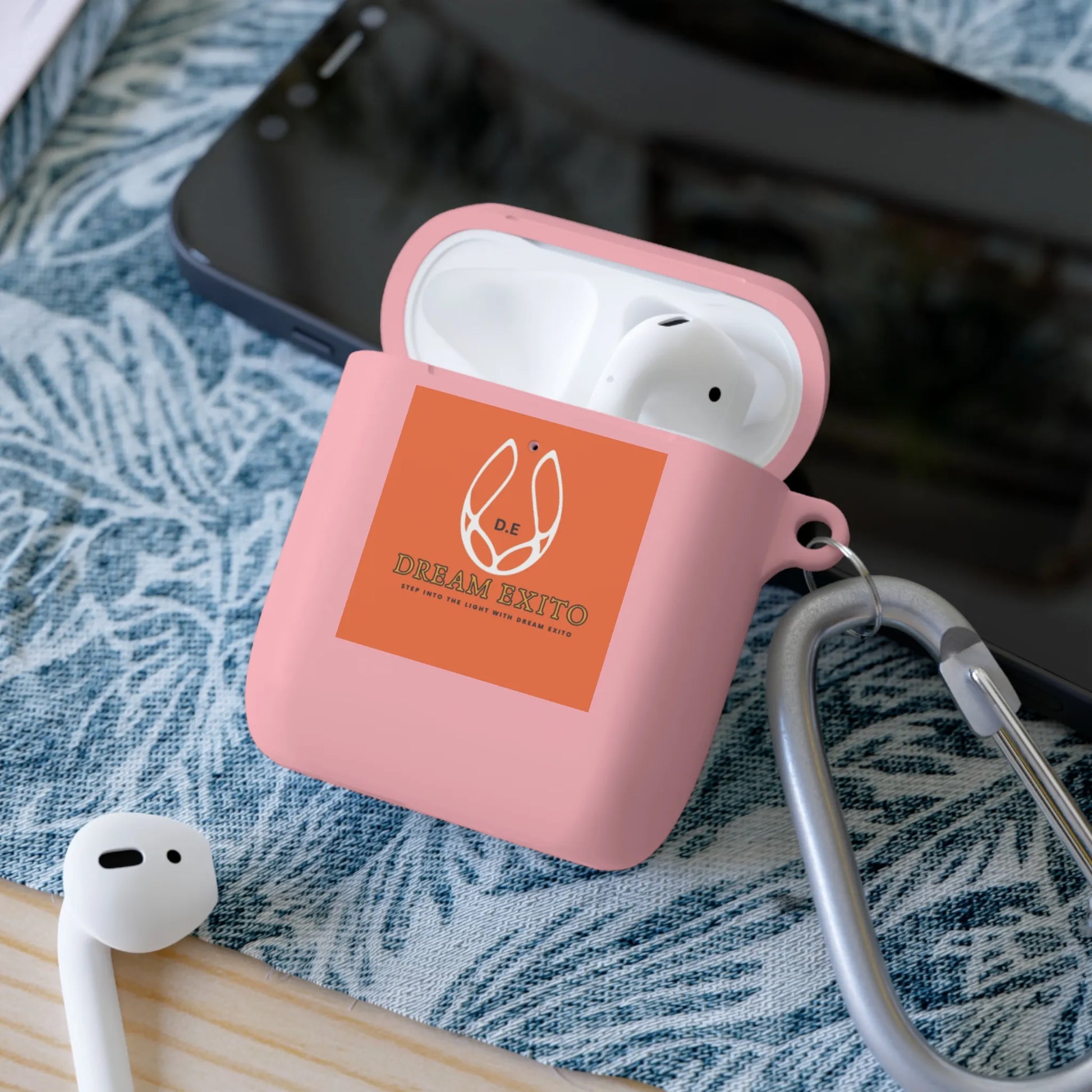 Pink earbud case with earbuds, label, and carabiner on fabric surface