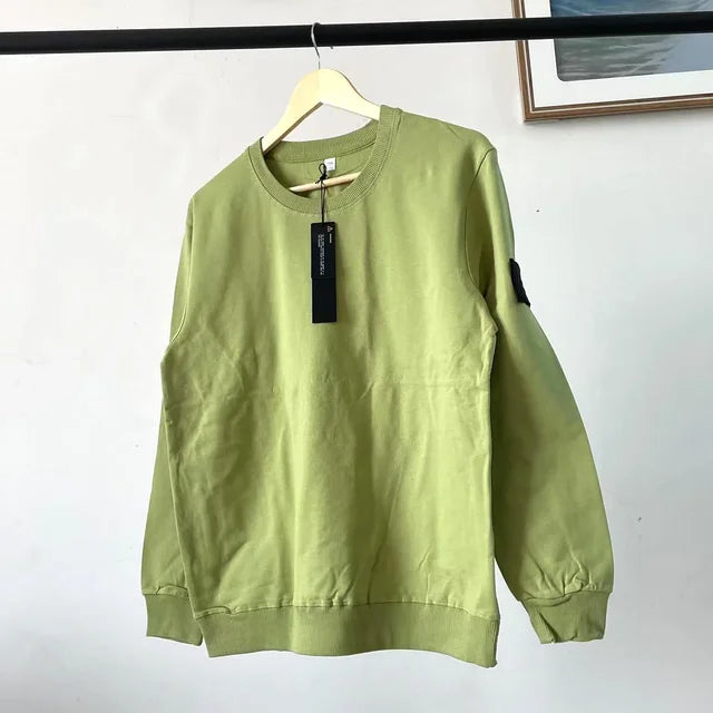 Sage green crewneck sweatshirt with black price tag and arm patch, hanging on wooden display hanger