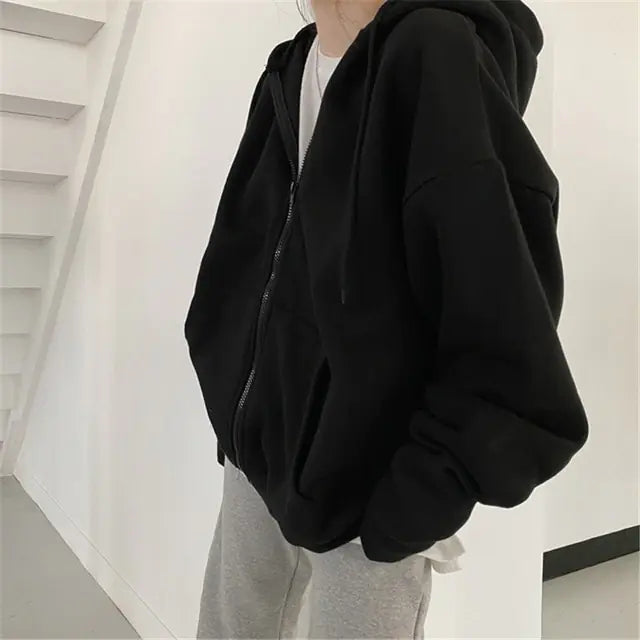 Side view of oversized black zip-up hoodie worn with light gray pants against white interior wall