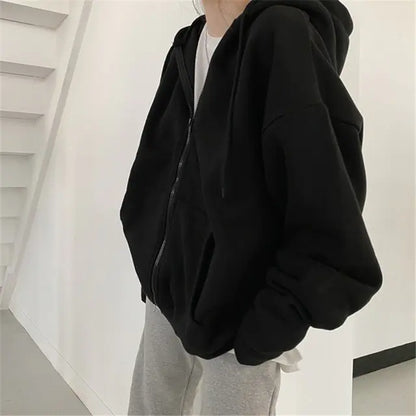 Side view of oversized black zip-up hoodie worn with light gray pants against white interior wall