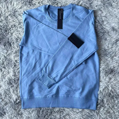 Sky blue cotton sweatshirt with black arm patch and price tag, displayed on gray textured surface