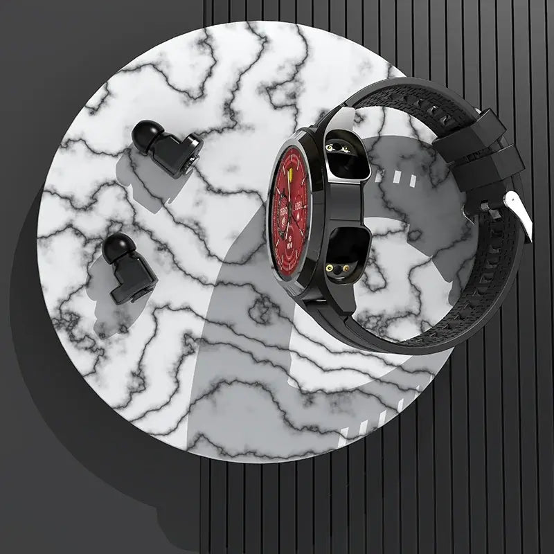 Smartwatch with a red face and black strap on a marble surface, accompanied by two black earbuds.
