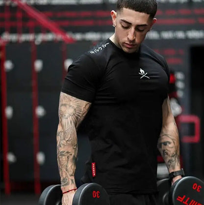 Tattooed athlete in black fitted shirt lifting dumbbells, logo visible on chest in gym setting