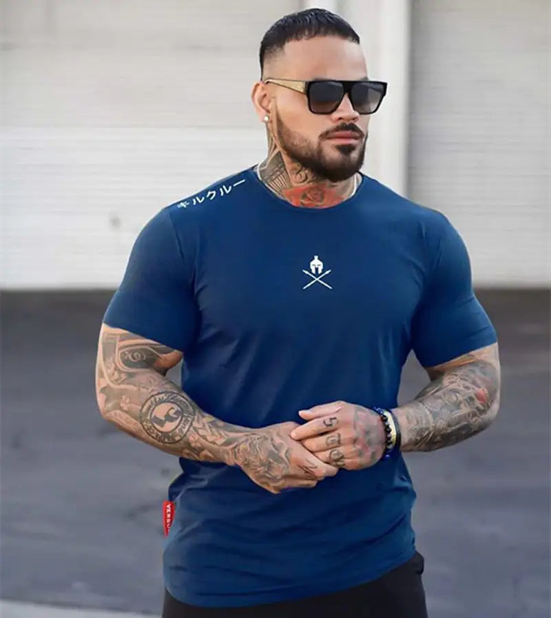 Tattooed model in navy blue fitted shirt wearing sunglasses, standing against concrete wall
