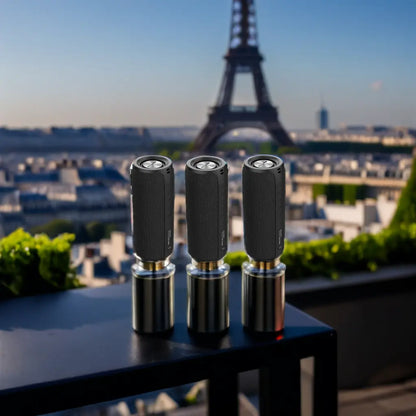 Three black cylindrical speakers on stands with the Eiffel Tower in the background.