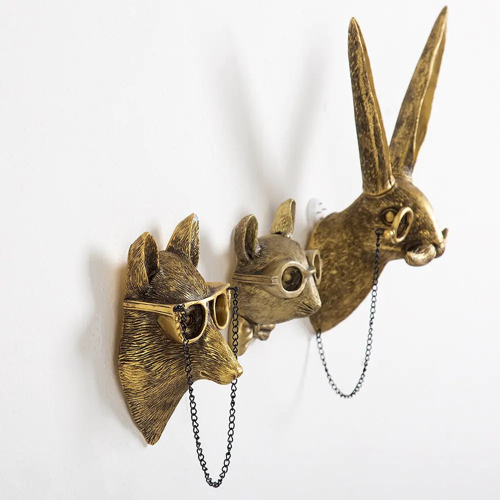 Three brass animal head sculptures with glasses mounted on a wall