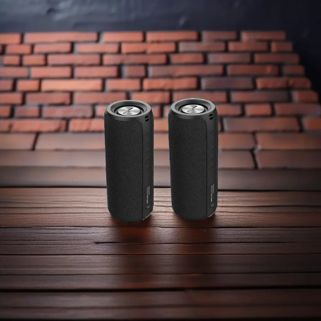 Two black cylindrical speakers on a wooden surface with a brick wall background.