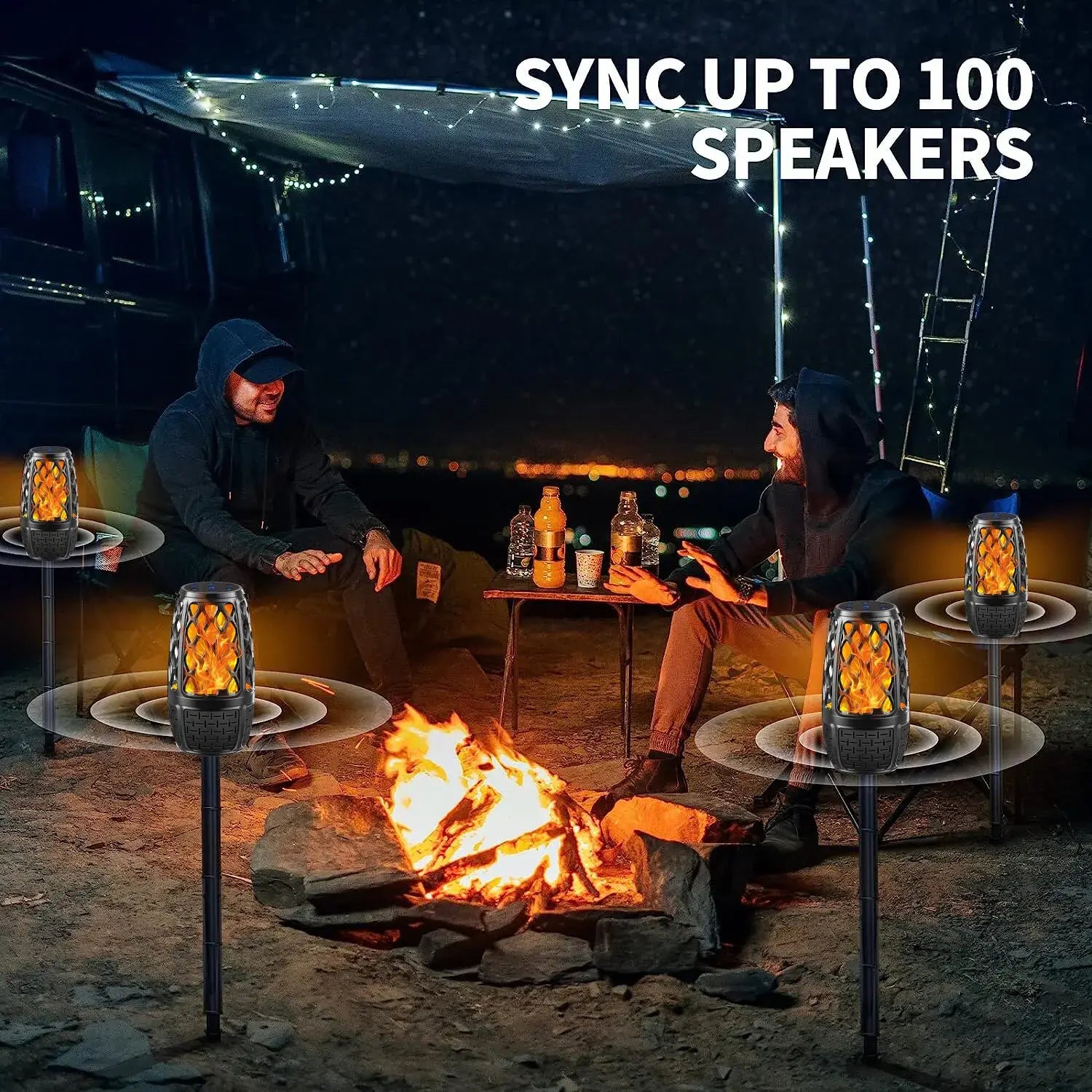 Two people sitting around a campfire at night with flickering torch-like speakers nearby.