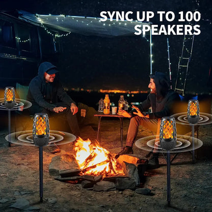 Two people sitting around a campfire at night with flickering torch-like speakers nearby.