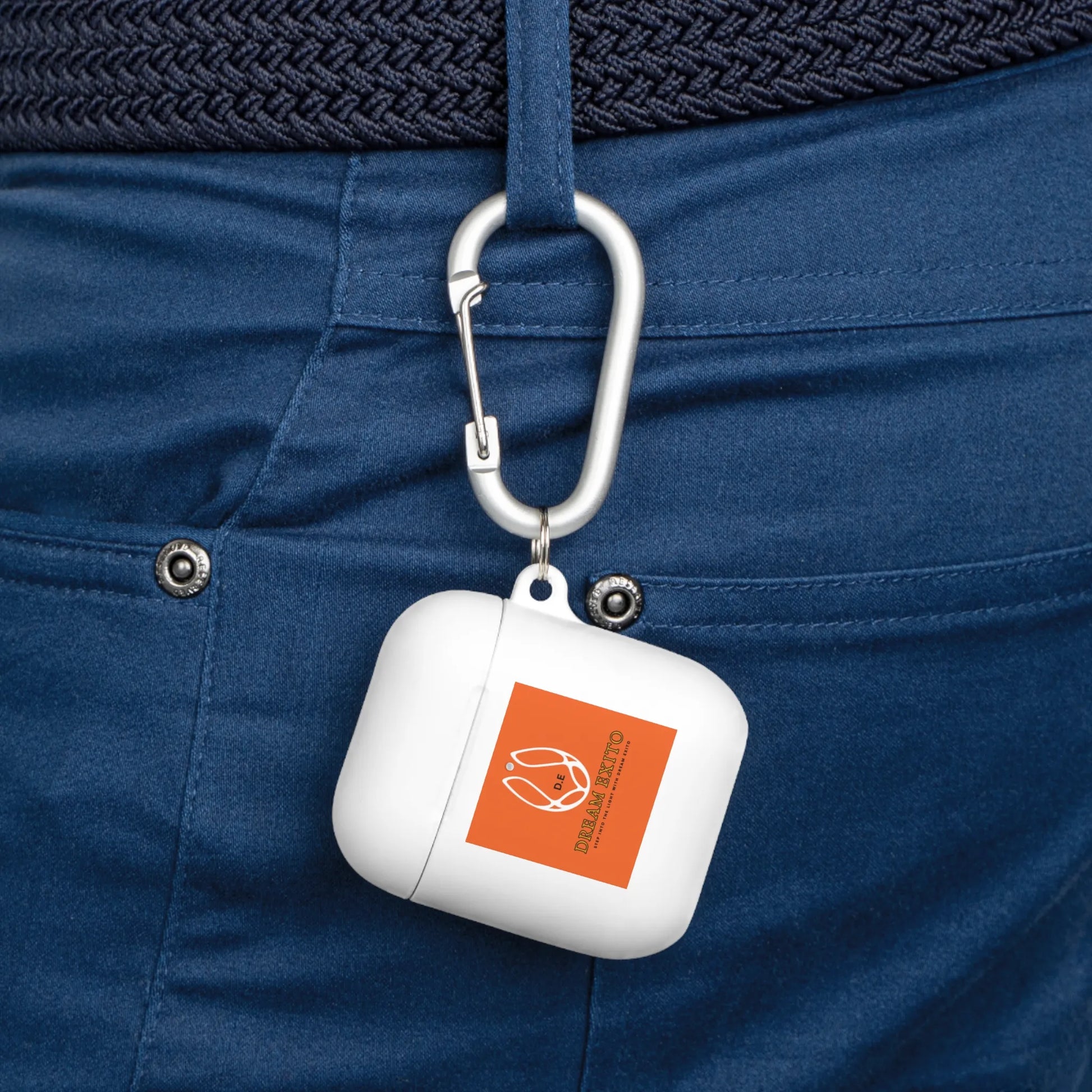 White AirPods case with an orange label attached to blue pants by a silver carabiner.