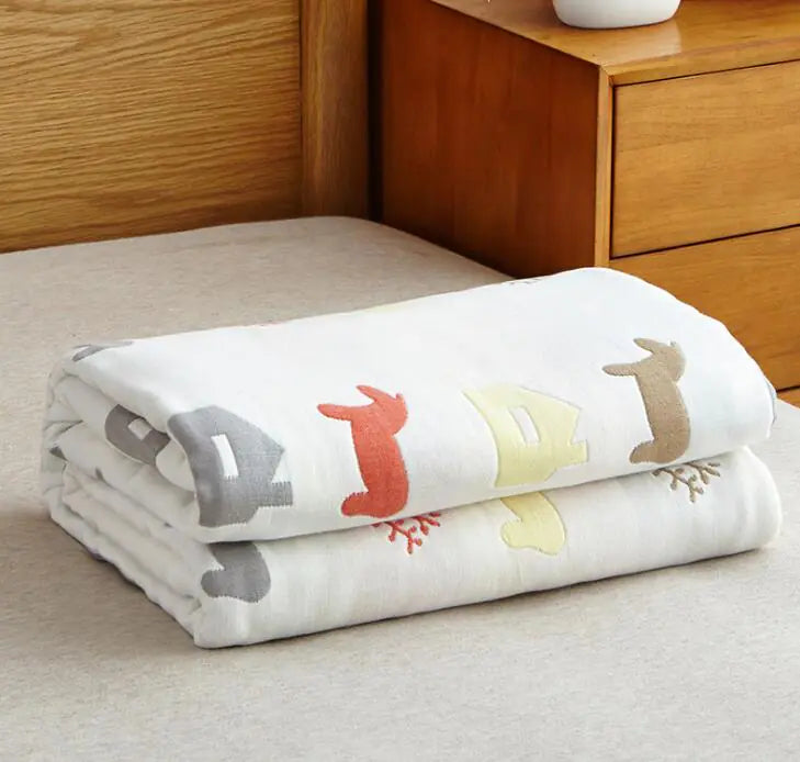 White blanket decorated with colorful animal silhouettes stacked on bed by wooden nightstand.