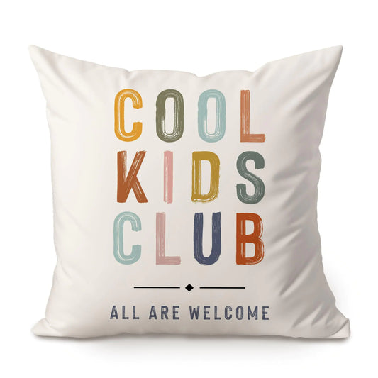 White decorative pillow with 'COOL KIDS CLUB—ALL ARE WELCOME' in colorful retro-style lettering on front